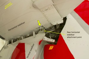 Horizontal-to-vertical stabiliser attachment with the aerodynamic fairings removed. View looking upwards at the underside of the horizontal stabiliser. The thick yellow arrow indicates cracking in the composite structure around the rear attachment point (Credit: ATSB)